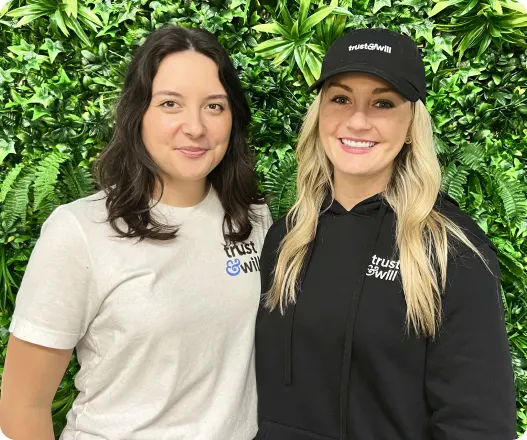 Two team members smiling together in front of a green wall representing legacy planning support